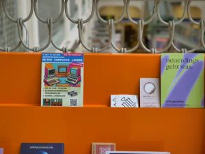 Orangefarbenes Informationsbrett mit Flyern zur Retro Computer Lounge und anderen kulturellen Angeboten.
