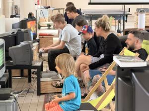 Gruppe von Erwachsenen und Kindern spielt gemeinsam Videospiele auf alten Röhrenfernsehern.