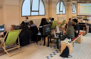 Gruppe spielt Videospiele an alten CRT-Monitoren in einem Raum mit Liegestühlen und Beamer-Projektion.
