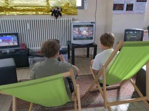 Zwei Jungen in grünen Liegestühlen spielen Videospiele auf alten Röhrenfernsehern.